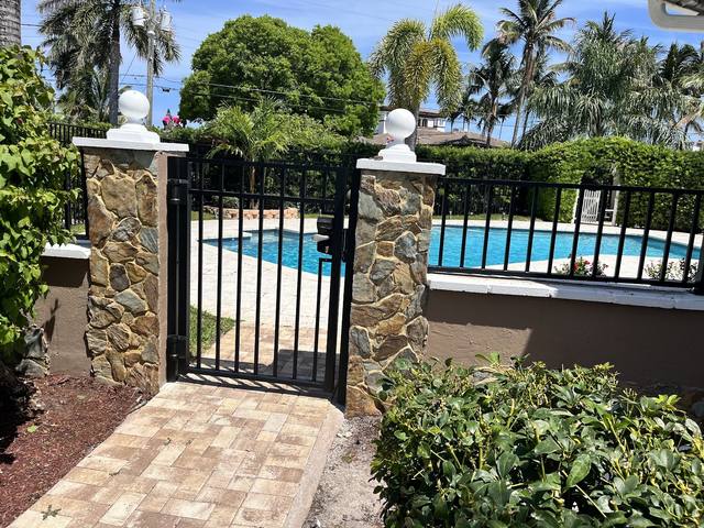 Black aluminum pool gate set between stone columns
